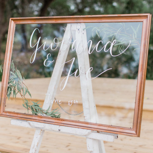 Clear Welcome Sign with White Writing And Greenery Details in Copper Frame at Park 31 by CalliRosa
